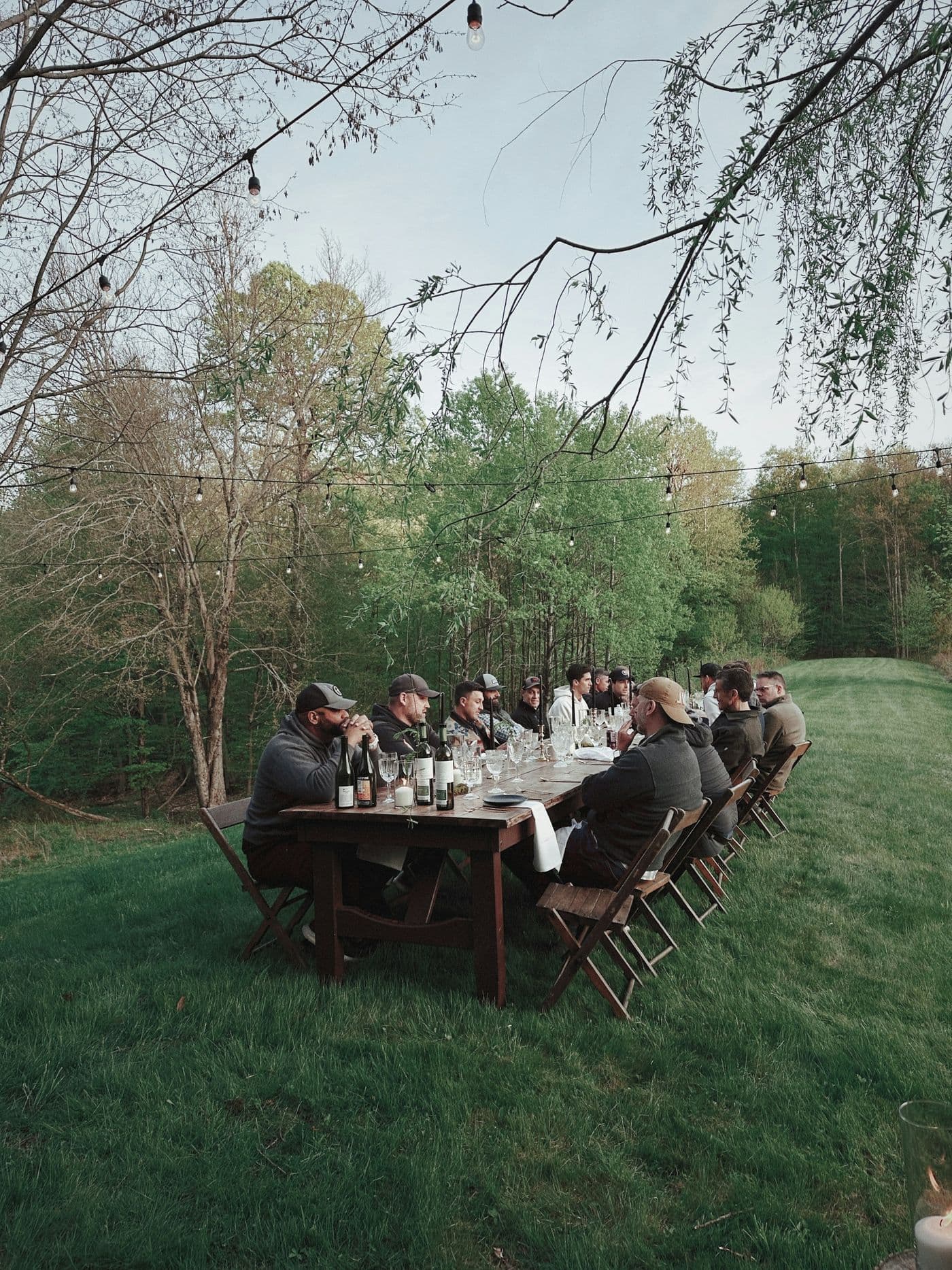 A long dinner table set outdoors under the trees